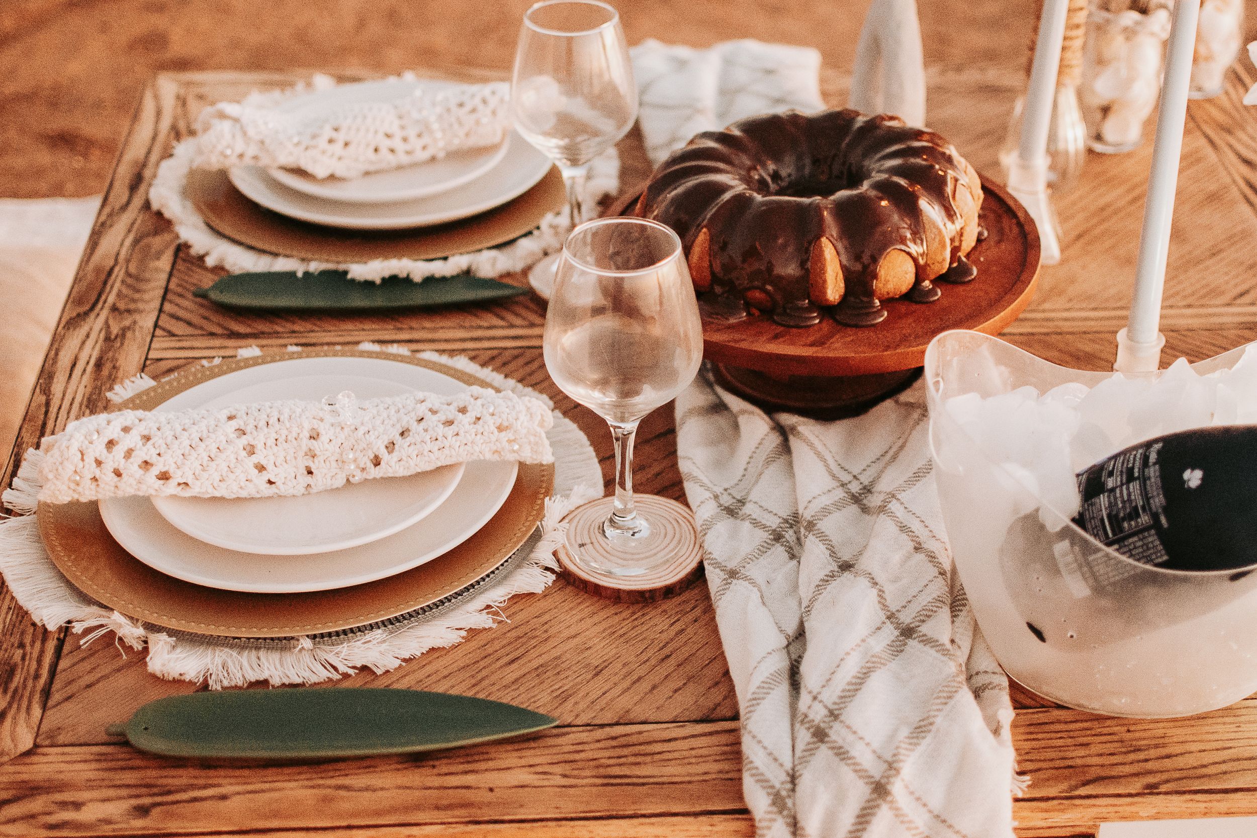 Rustic table setting with white plates, glasses and textured linens in warm lighting.