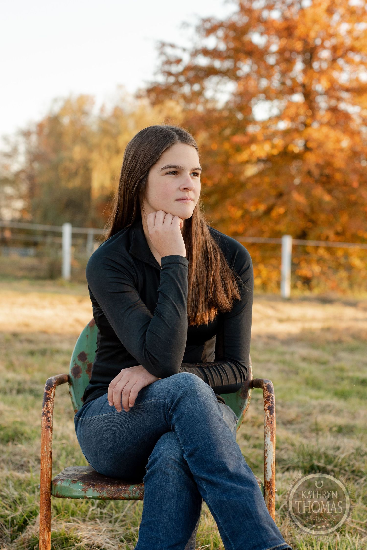 Thoughtful pose on vintage chair with fall colors in background.