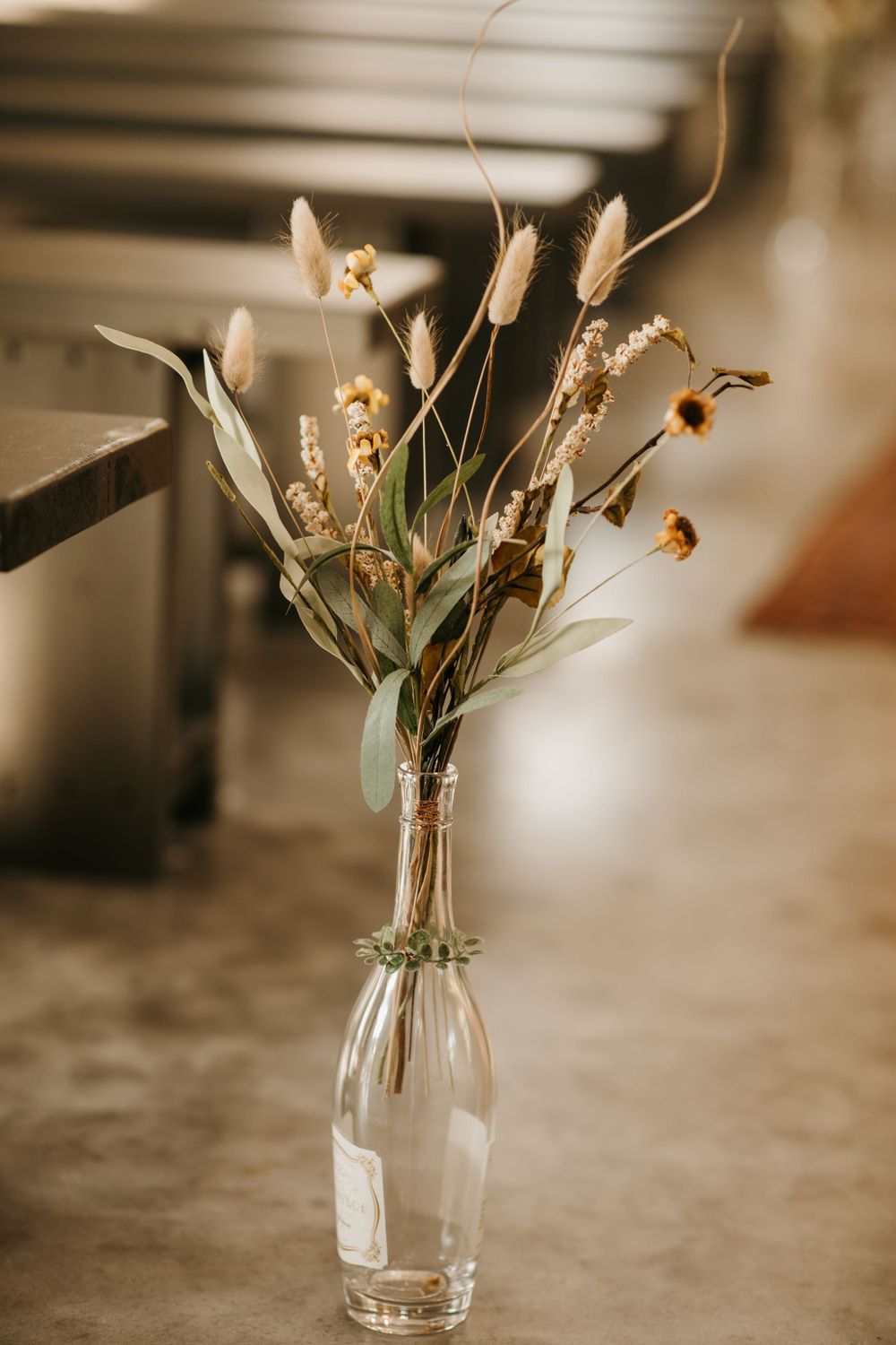 Elegant dried wildflower arrangement in clear glass bottle decorates wedding ceremony aisle.