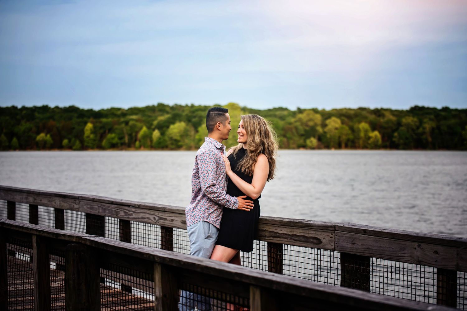Couple embracing on wooden dock overlooking serene lake at sunset.
