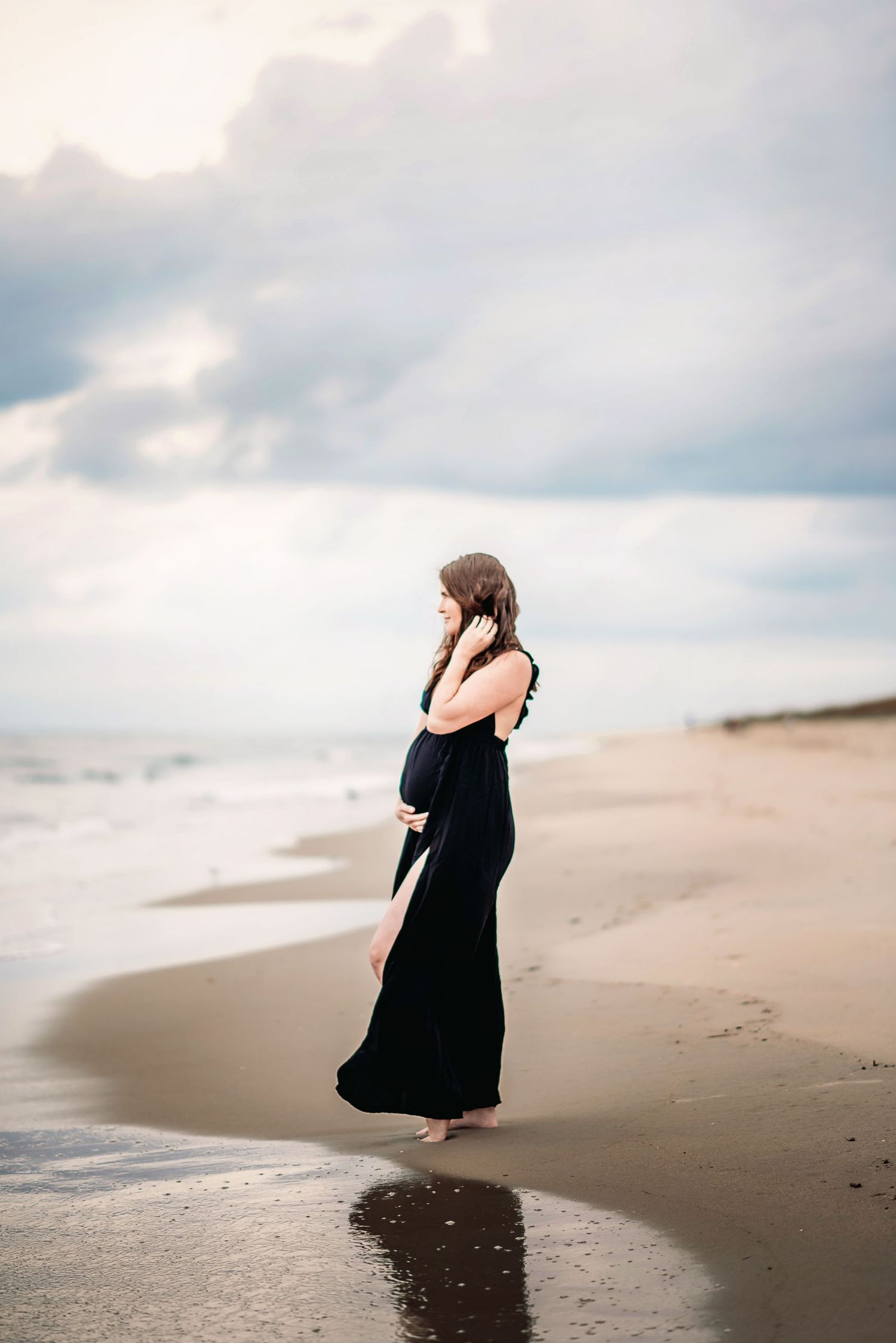 a maternity photo of a pregnant woman in a black dress on the beach