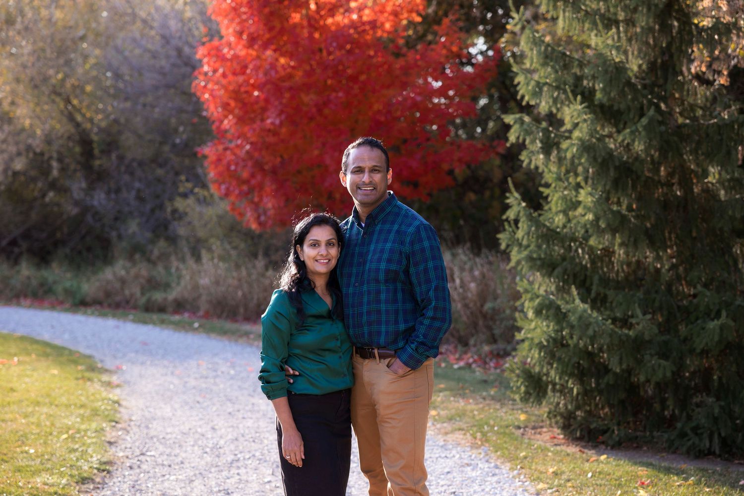 Two people standing on path with bright red maple and evergreen trees in background.