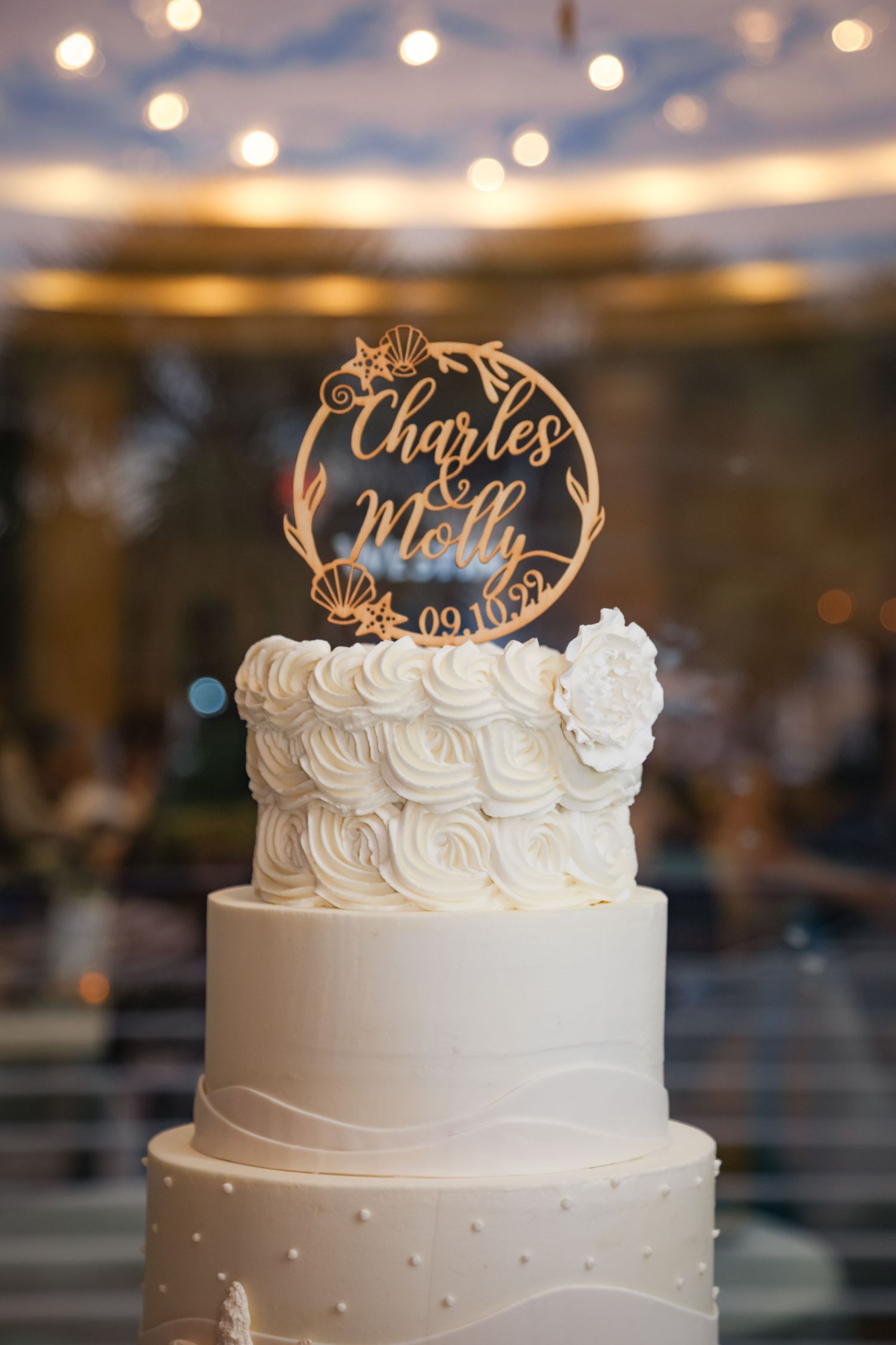 An elegant white wedding cake with rose piping and a custom name topper.