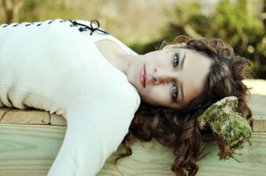 Dreamy portrait with long wavy hair lying on wooden surface in natural light.