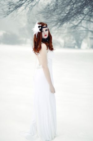 Ethereal winter portrait featuring a white gown and flowing red hair against a snowy forest backdrop.