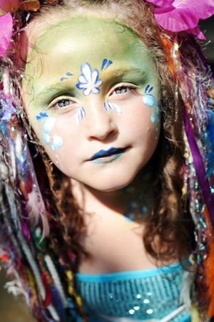 Ethereal fantasy makeup with blue flowers and green face paint in artistic portrait.