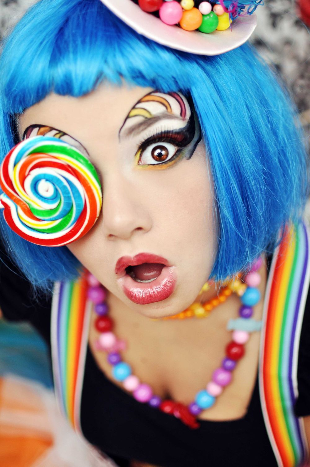 Candy-themed costume with bright blue hair, colorful makeup and a lollipop prop.