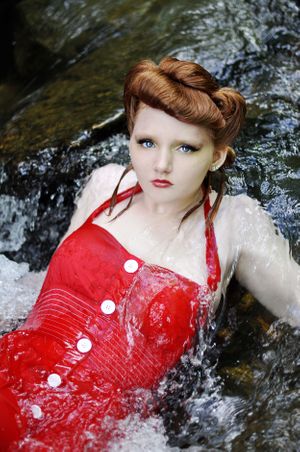 Fashion model in vintage-style red swimsuit with white buttons poses in flowing water.