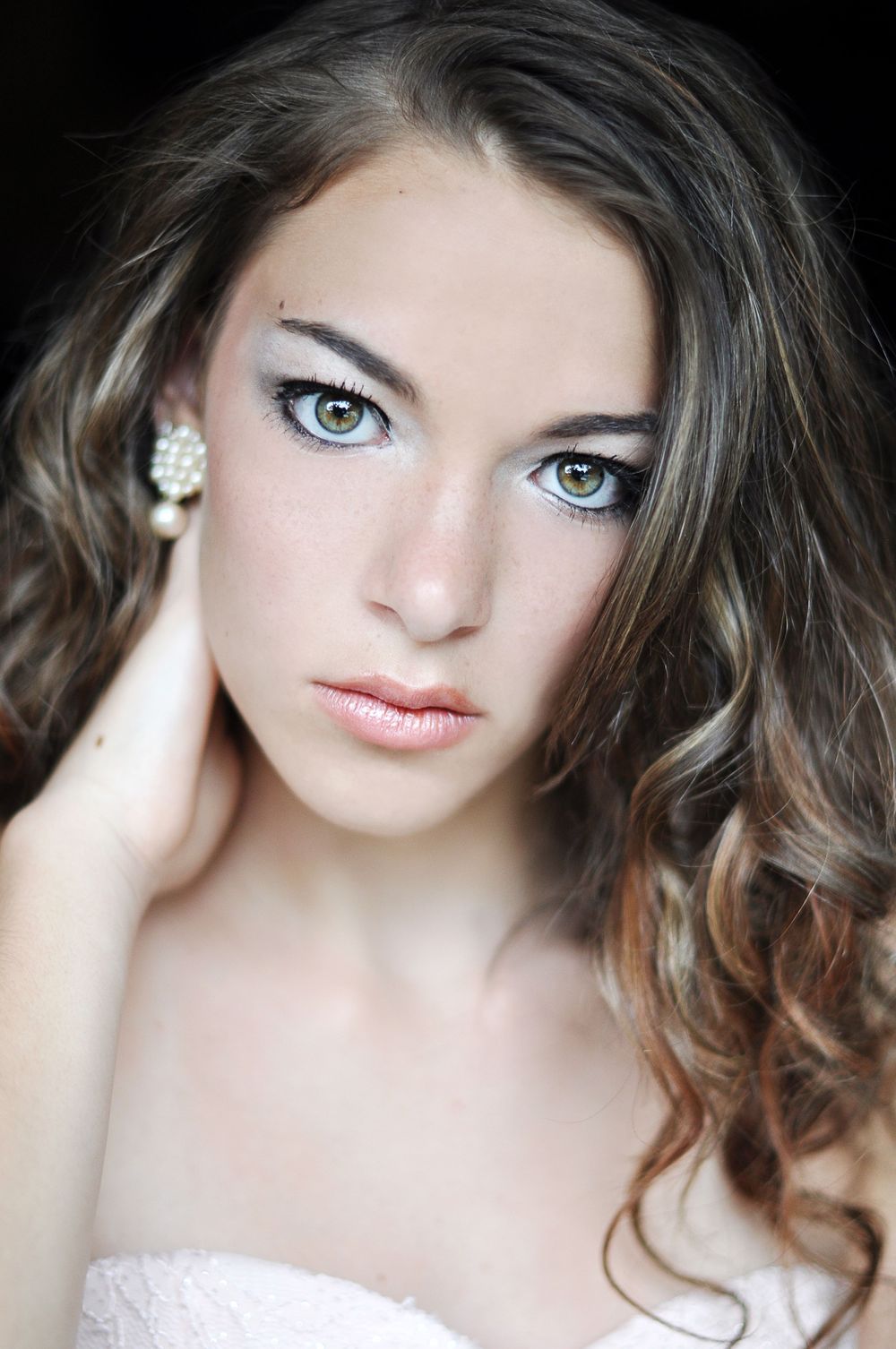 Soft portrait with natural makeup and curled hair against light background.