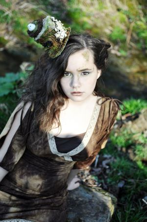 Fantasy portrait with vintage dress and ornate headpiece in garden setting.