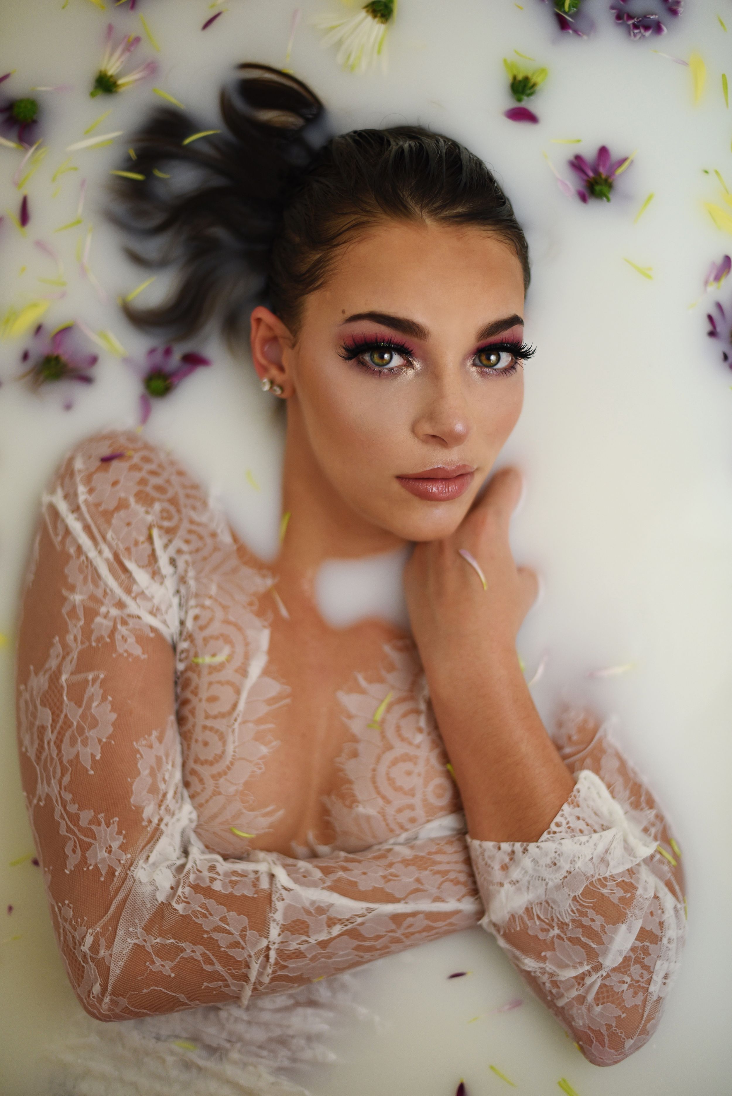 Artistic beauty portrait with delicate lace sleeves surrounded by scattered purple flower petals.