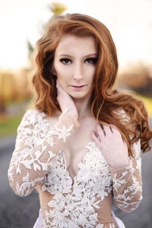 A woman wearing a delicate white lace dress with long sleeves poses outdoors at sunset.