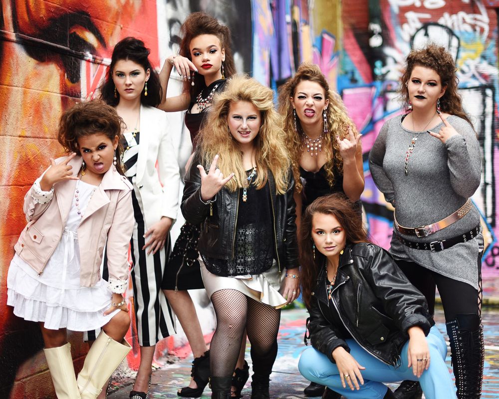 Group in edgy punk rock fashion poses against colorful graffiti wall.
