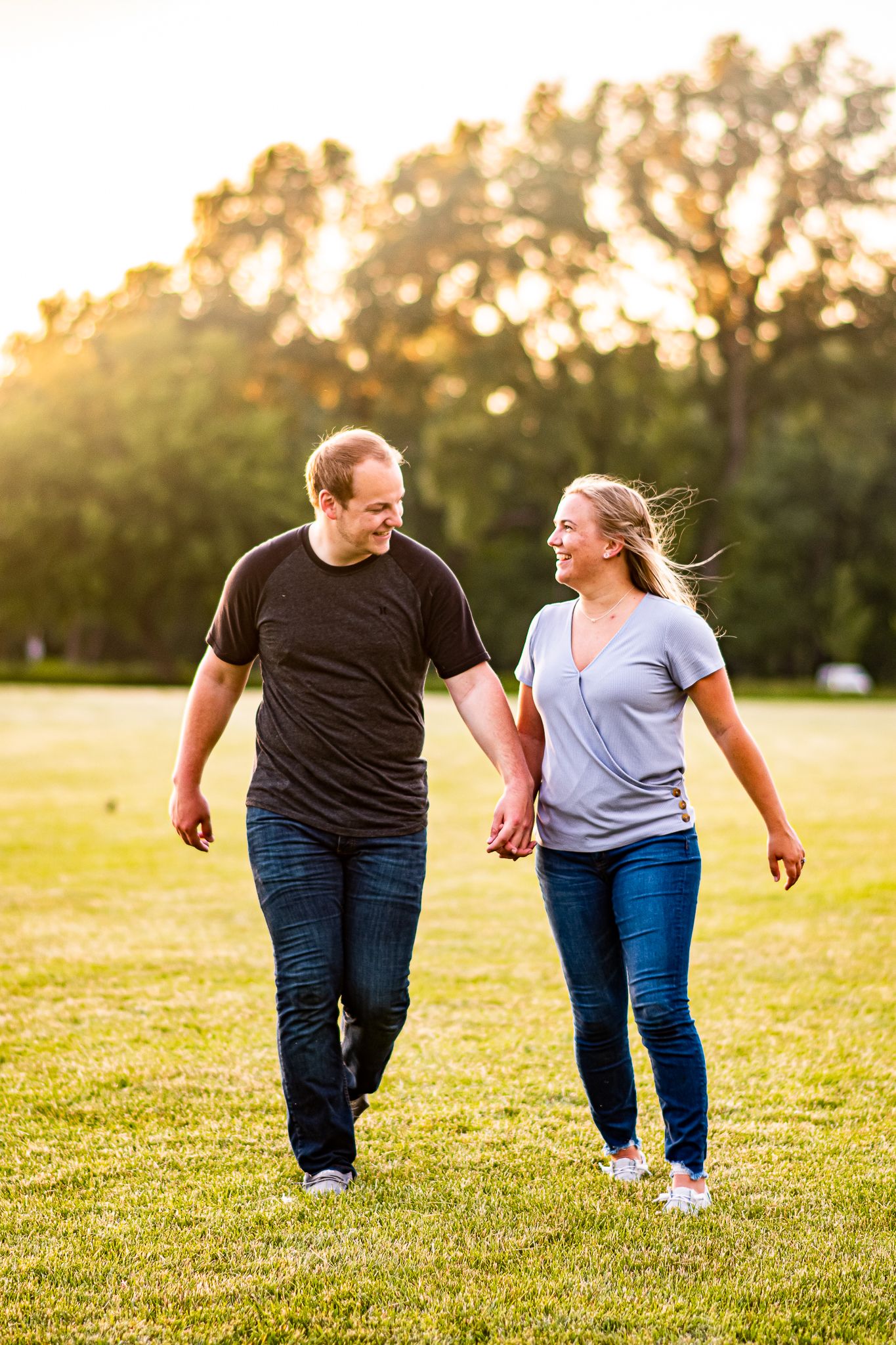 A couple walking hand in hand through a grassy field at sunset.