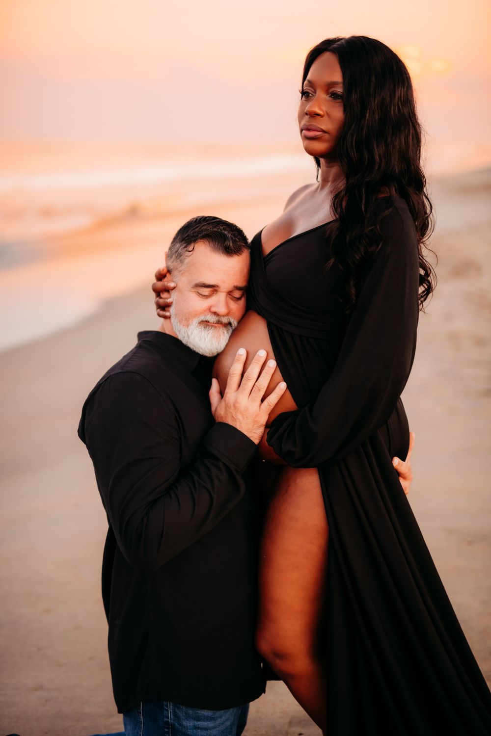 Intimate maternity portrait of couple embracing on beach at sunset.