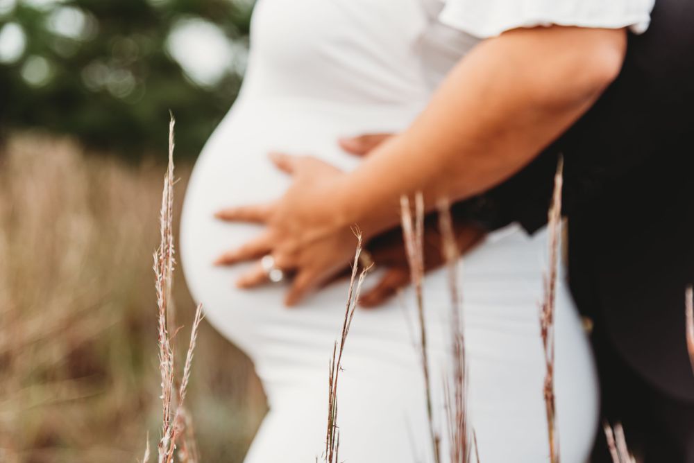 Close-up of pregnant belly with dried grass in foreground.