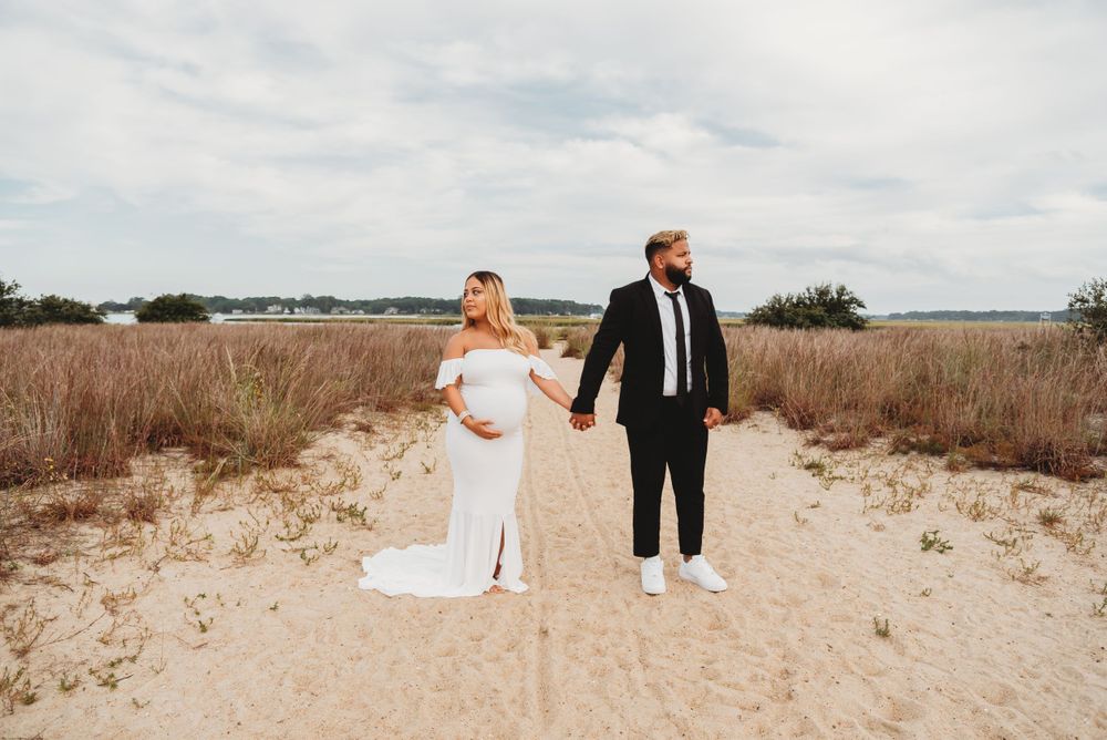 A couple poses together on a sandy beach path surrounded by tall grass.