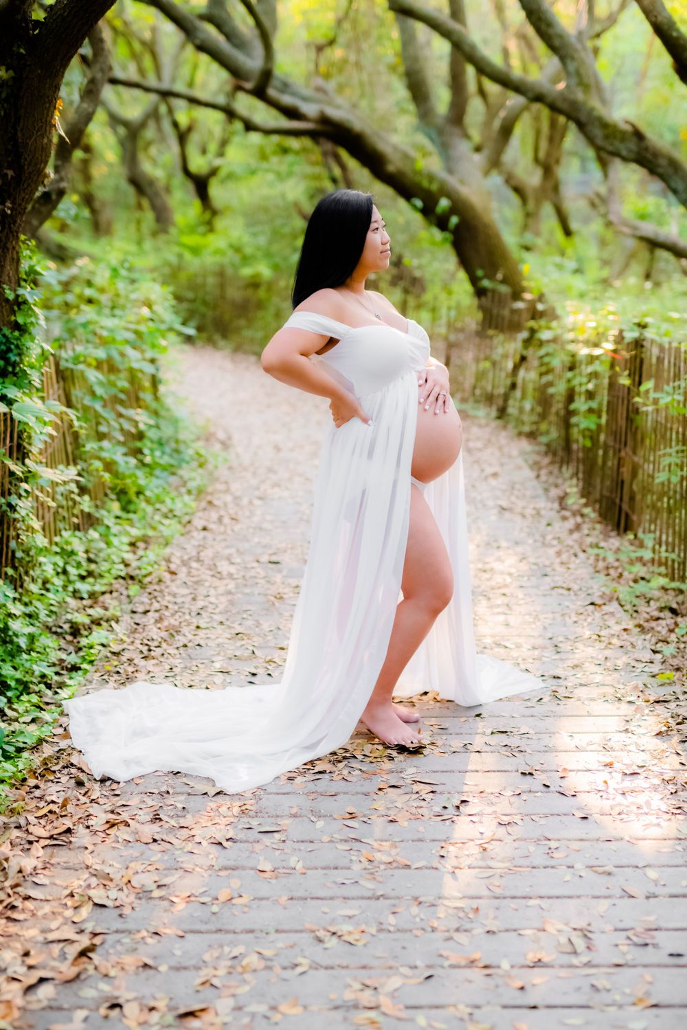 A stunning pregnancy photoshoot on a wooden walkway surrounded by lush greenery and draped in flowing white fabric.