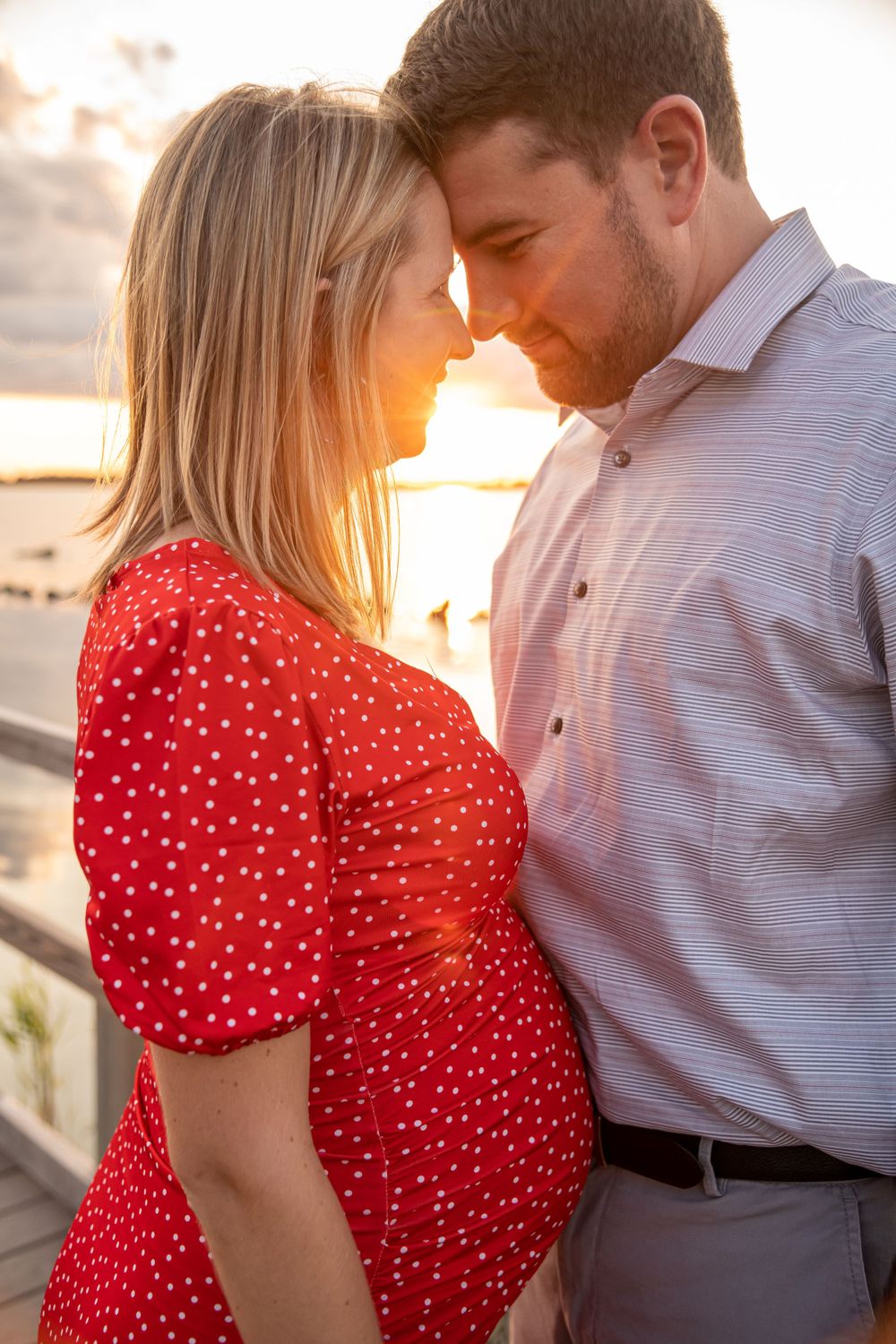 An intimate maternity portrait at sunset with a red polka dot dress against wooden railings.
