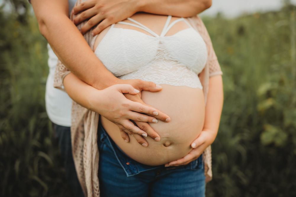 Close up of hands cradling pregnant belly against natural outdoor backdrop.