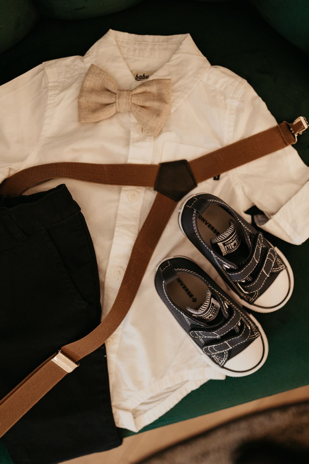Baby outfit layout with white onesie, brown suspenders and tiny black shoes.
