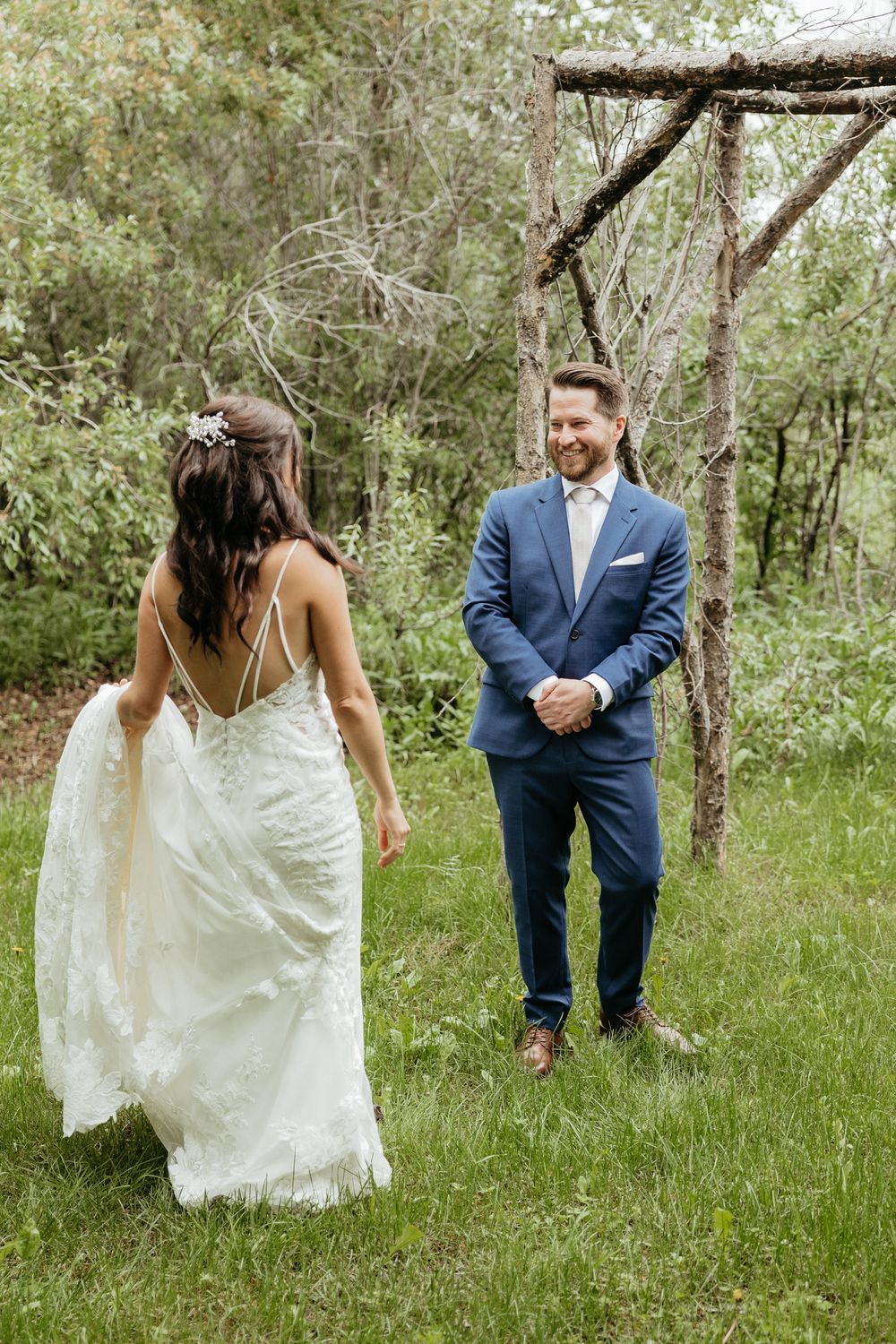 A couple in wedding attire playfully dances together in a lush green forest setting.