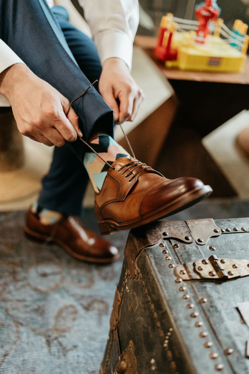 Close-up of brown leather dress shoes being laced up on textured surface.