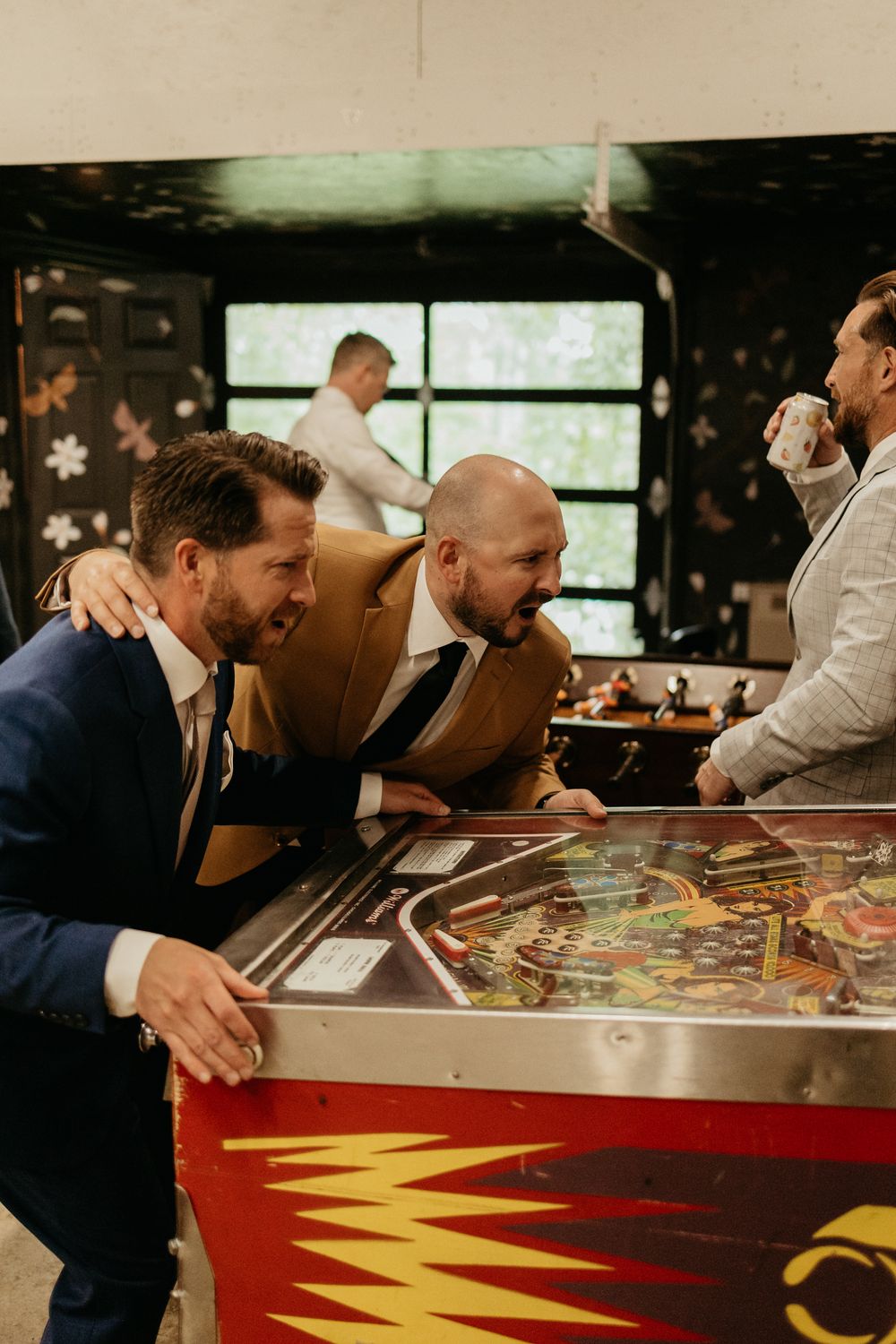 Group playing pinball machine together at casual gathering.