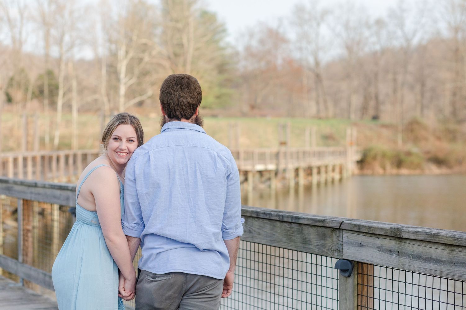 A couple shares a romantic moment on a wooden bridge overlooking a serene lake in early spring.