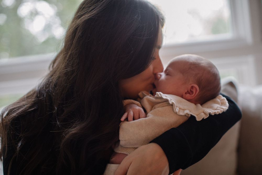 A mother with long dark hair tenderly kisses her newborn baby while cradling it gently in her arms.
