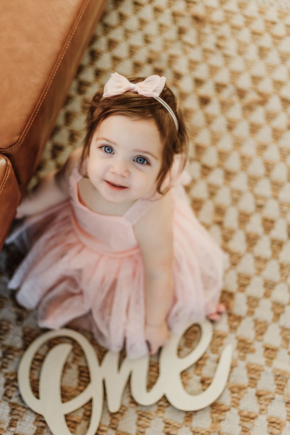 Baby in pink tulle dress sits on patterned carpet next to decorative text.