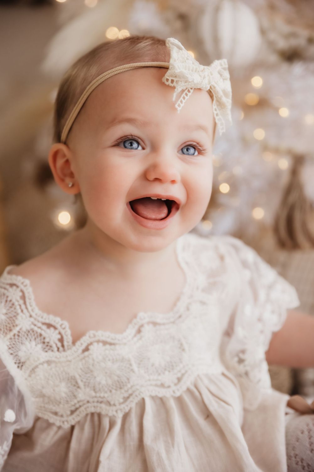 Baby in vintage lace dress smiling with bokeh lights in background.