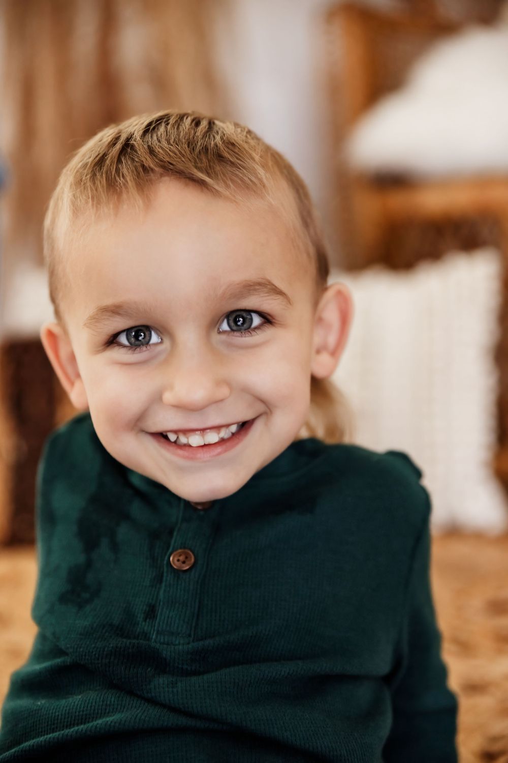 Child wearing dark green sweater smiles warmly indoors.