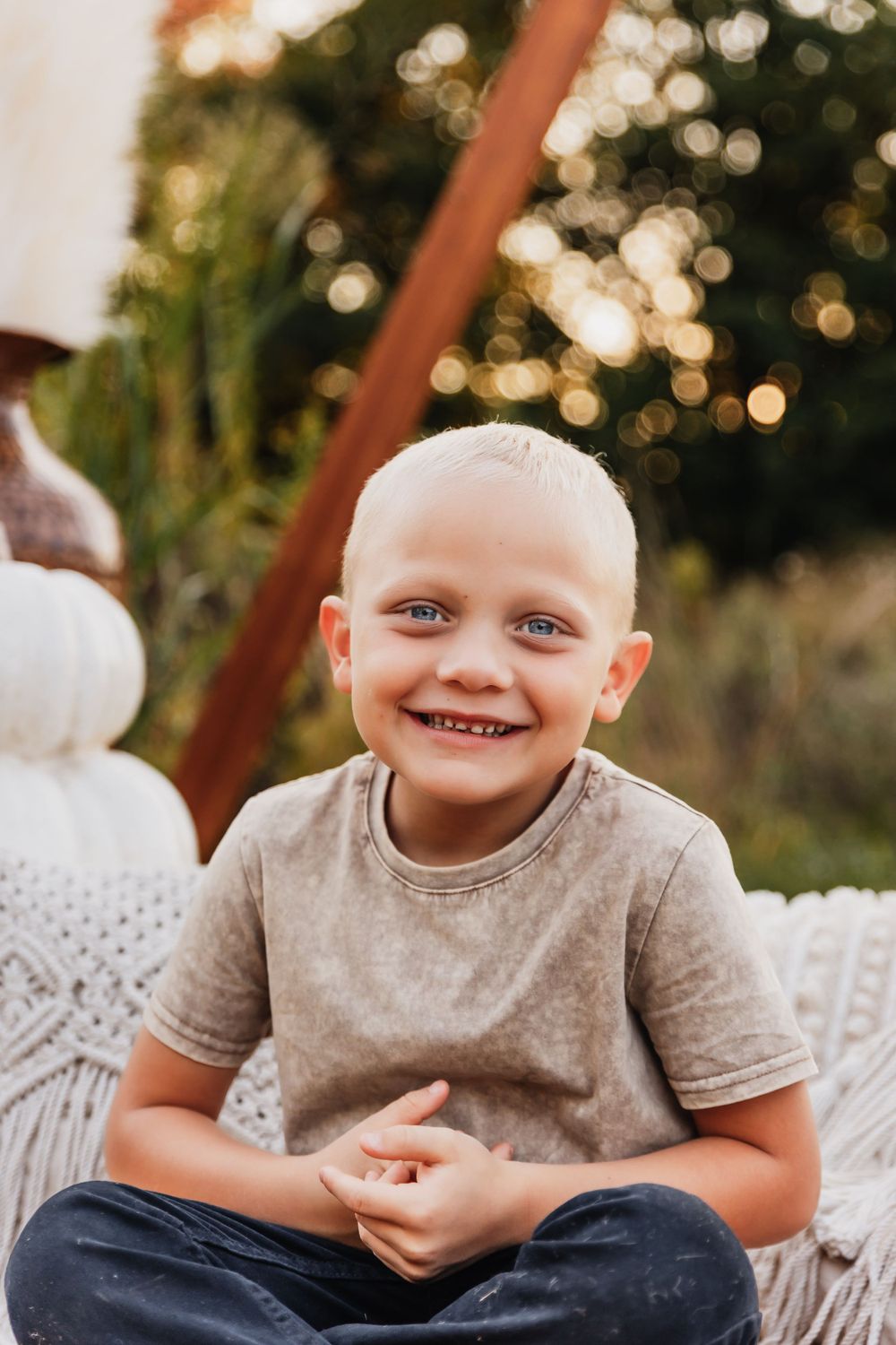A casual outdoor portrait of a child in a beige t-shirt sitting on white cushions.