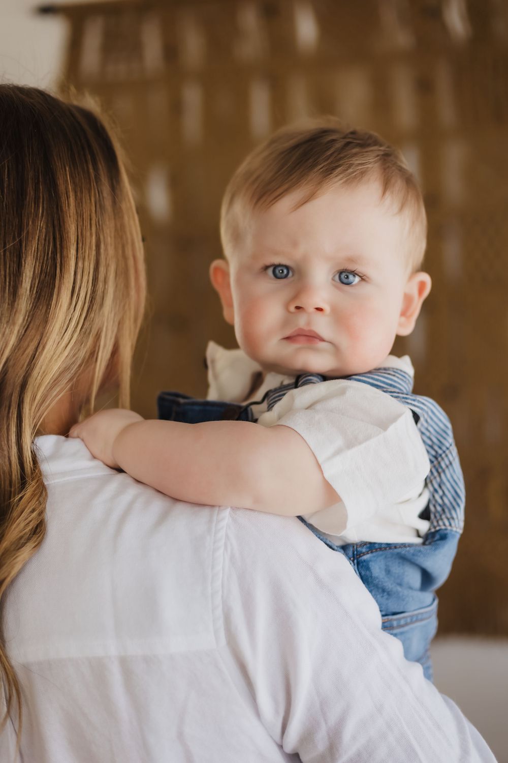 Baby in blue and white outfit being held against warm indoor setting.