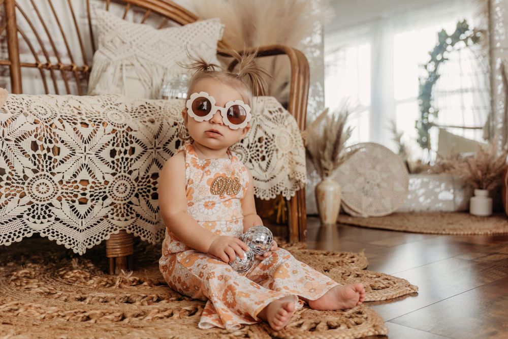 Baby plays on floor during birthday photoshoot with vintage-style decorations.
