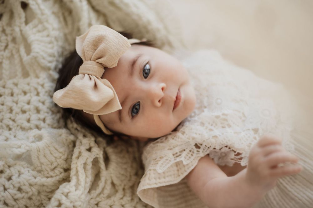 Child in cream sweater lying on textured beige blanket.