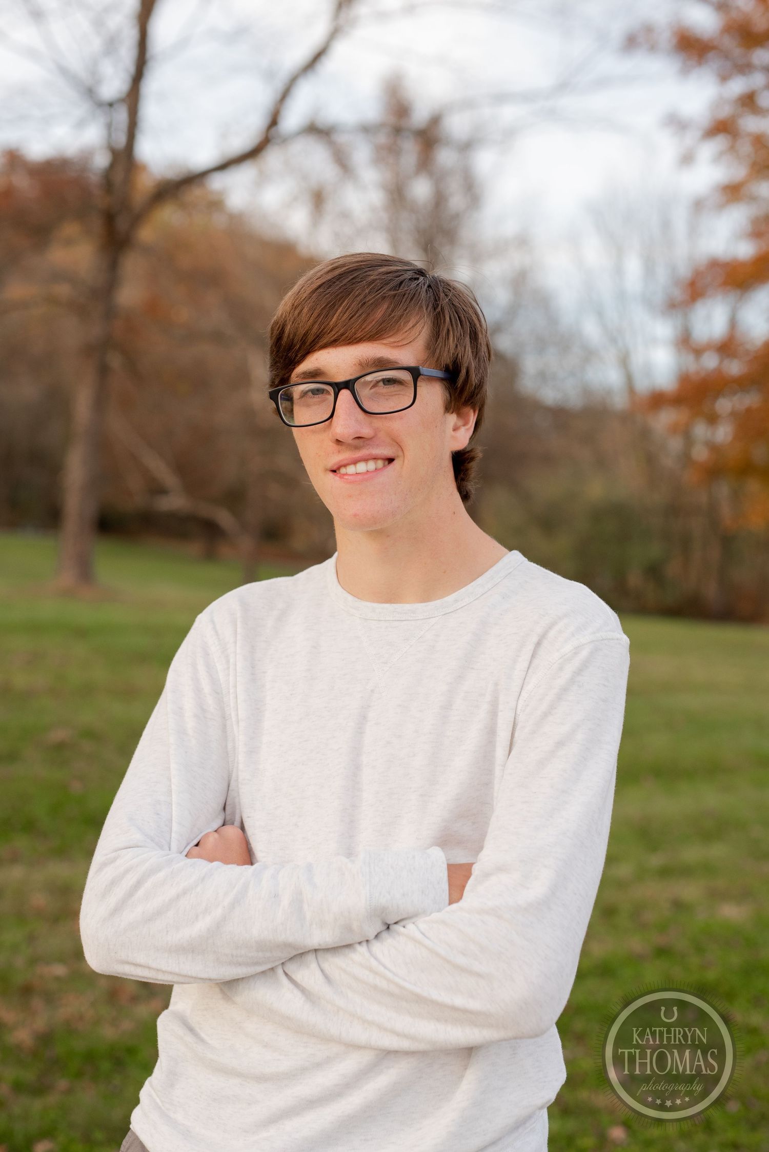Portrait of a student in glasses and white sweater smiling outdoors during autumn.