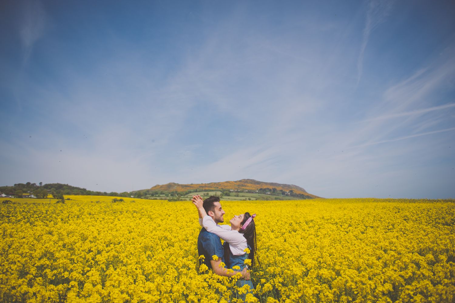 Couple hugging each other in the middle of a big field of yellow flowers