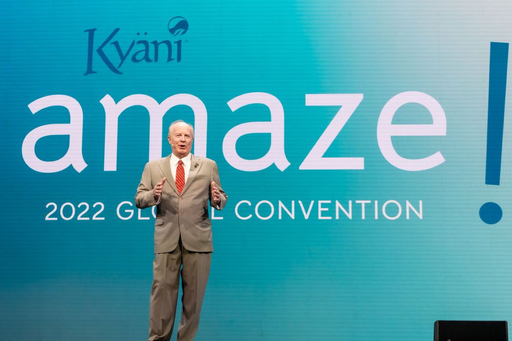 Kyani Amaze convention presenter speaking on stage with branded backdrop.