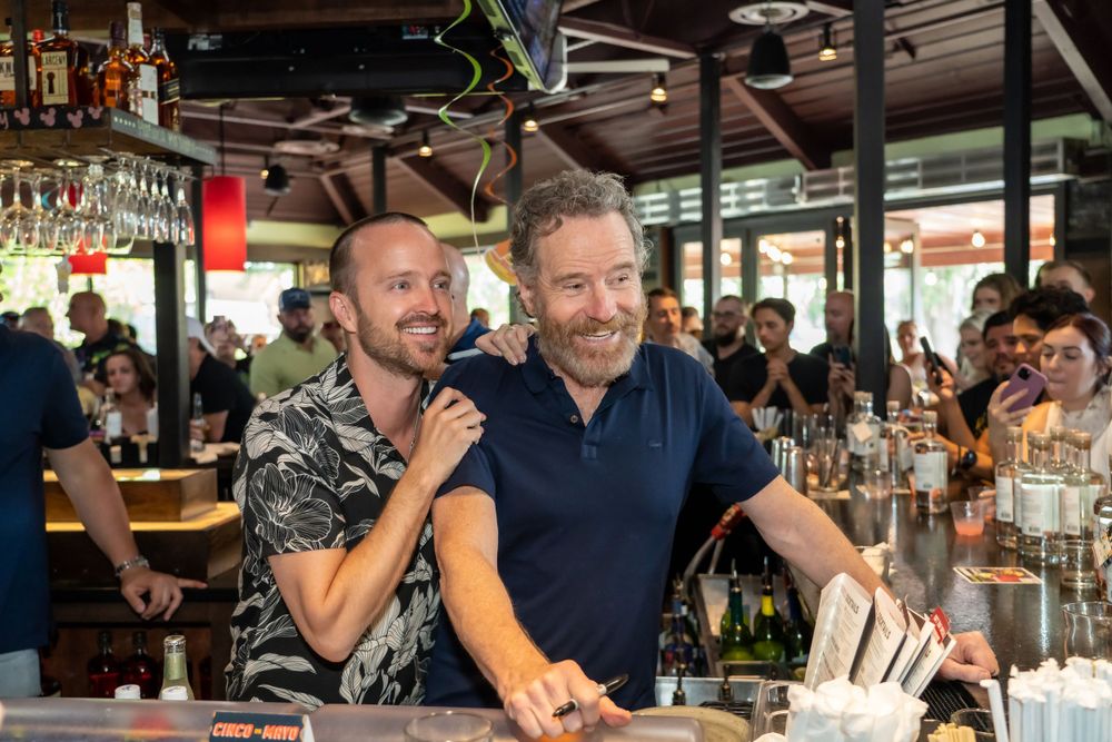 Two people behind bar counter smiling and interacting with customers.
