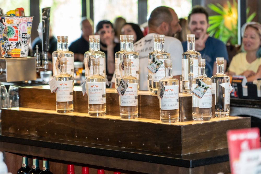 Multiple clear glass bottles arranged on a wooden display stand at a bar counter.