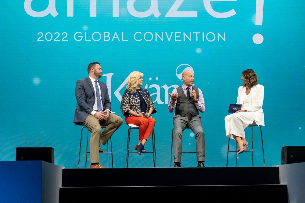 Panel discussion on stage with speakers seated against teal backdrop at Amaze 2022 Global Convention.