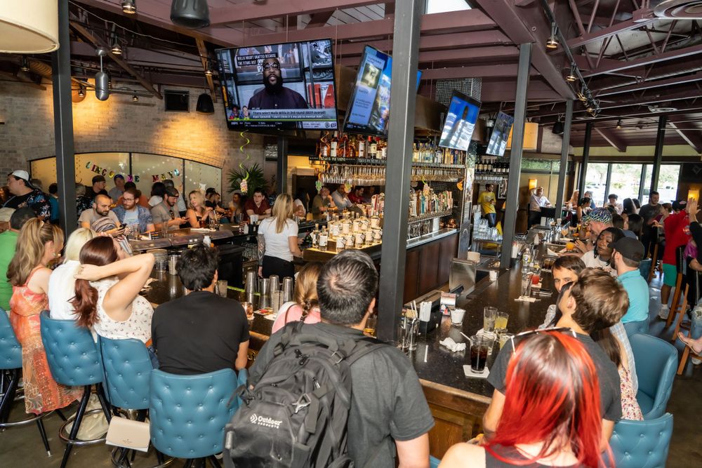Crowded bar filled with patrons watching TV screens mounted on walls.