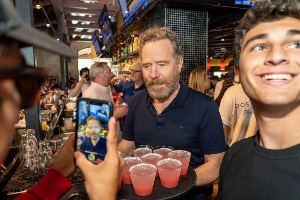 Customers at a busy bar holding pink cocktails while taking photos.