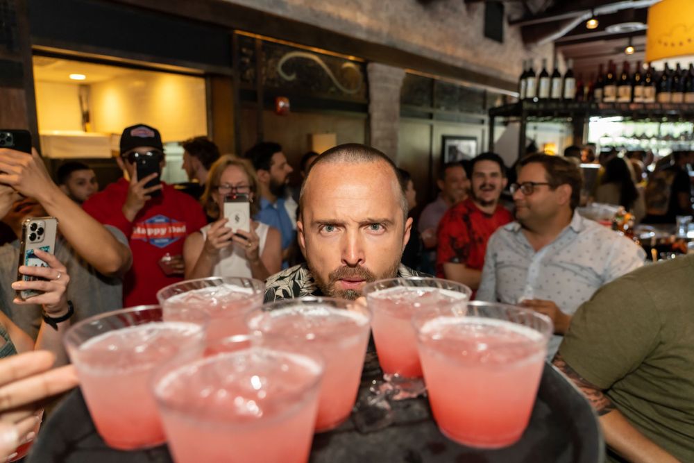 Person behind bar with multiple pink cocktails arranged on serving tray.