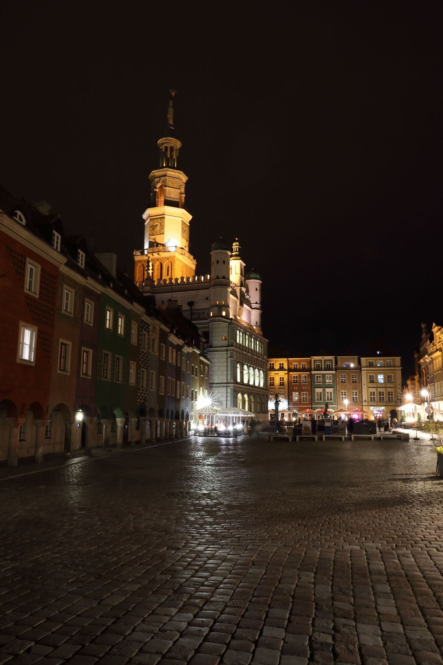 Illuminated historic town hall and market square at night in European city.