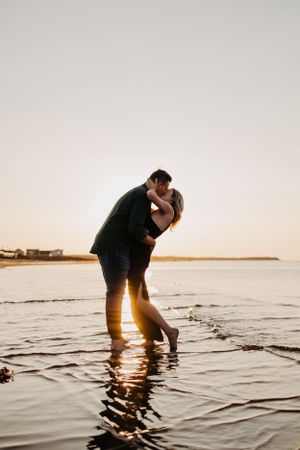 Silhouettes playing in shallow water during golden sunset at the beach.