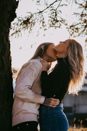 Two people share an intimate moment under tree branches at sunset.