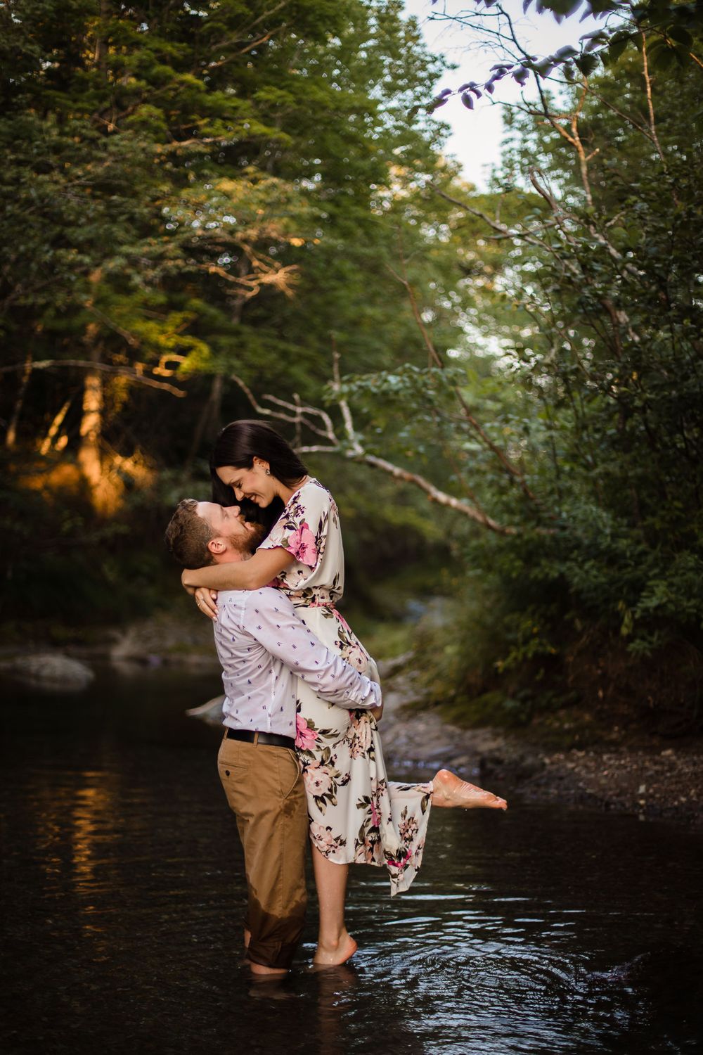 A romantic couple embraces while standing in a creek surrounded by forest at sunset.